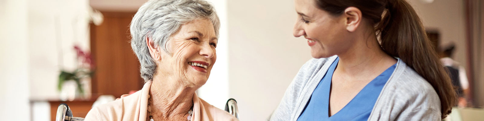 Female senior living resident smiling at female nursing assistant