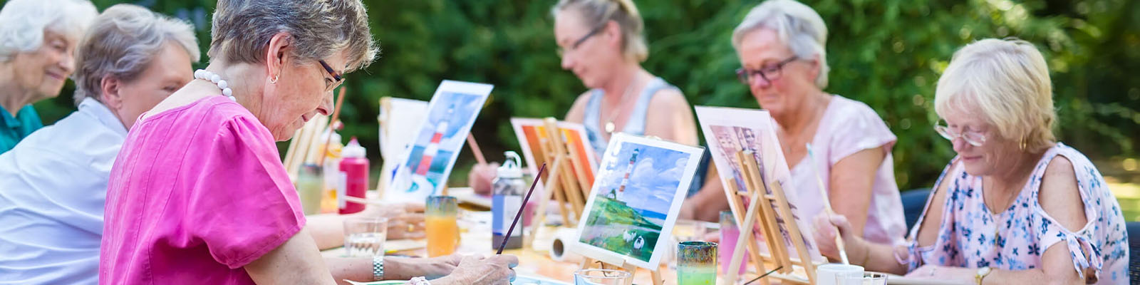 Group of female senior living residents sitting outdoors at a table for a painting activity