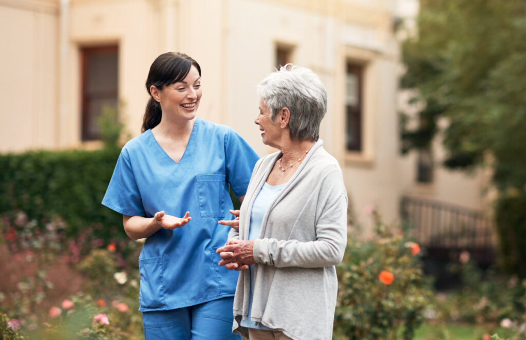 A female senior living resident walking outdoors with a female nursing assistant